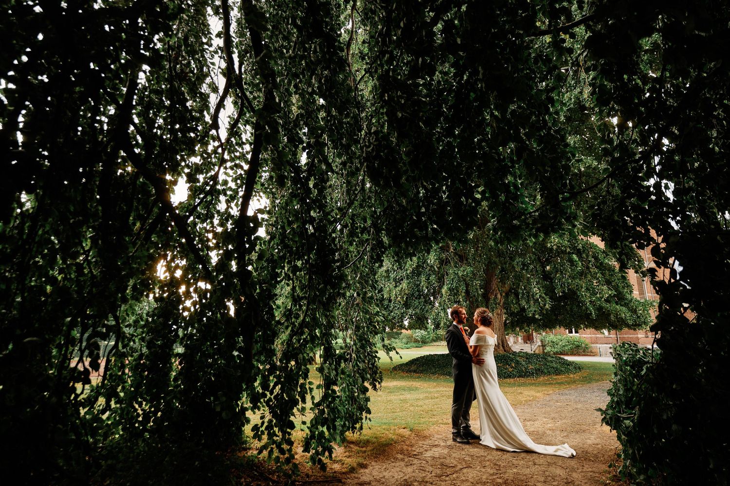 A couple shares a romantic moment under a weeping willow tree in an outdoor garden setting.