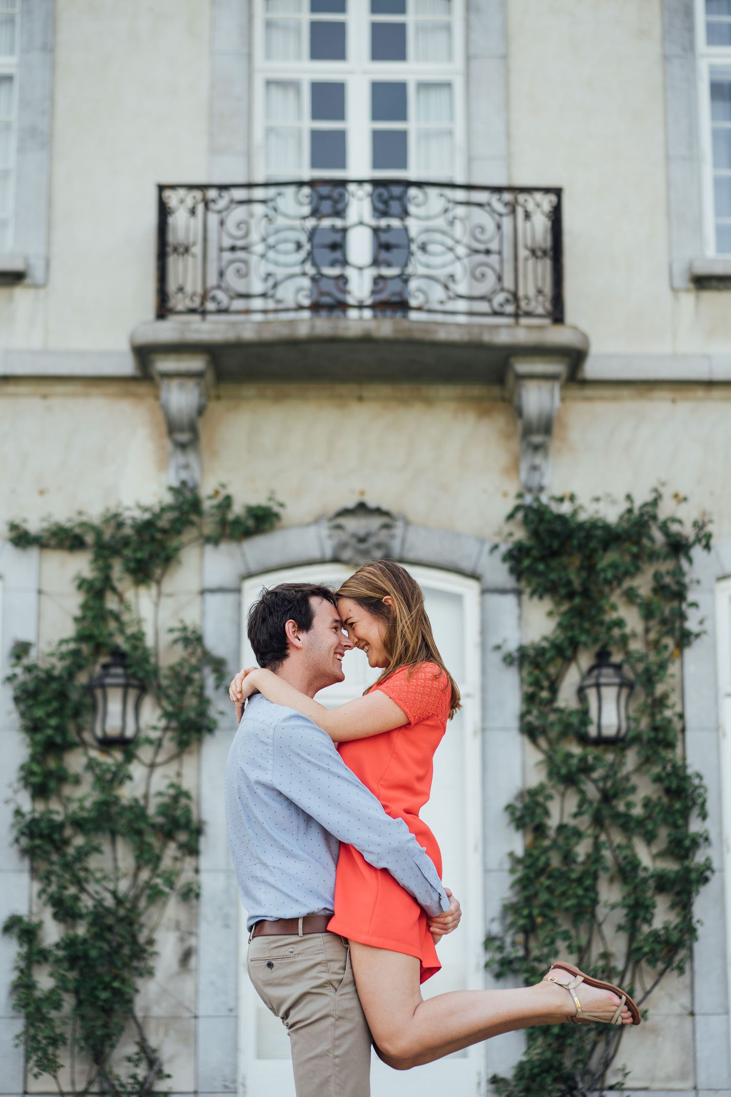 A couple embraces romantically in front of an elegant building with climbing vines and ornate balconies.