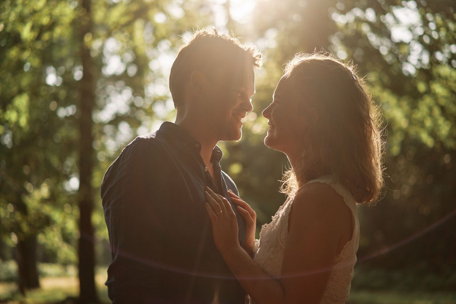 Silhouetted figures embrace in golden sunlight with trees and foliage creating a dreamy outdoor backdrop.