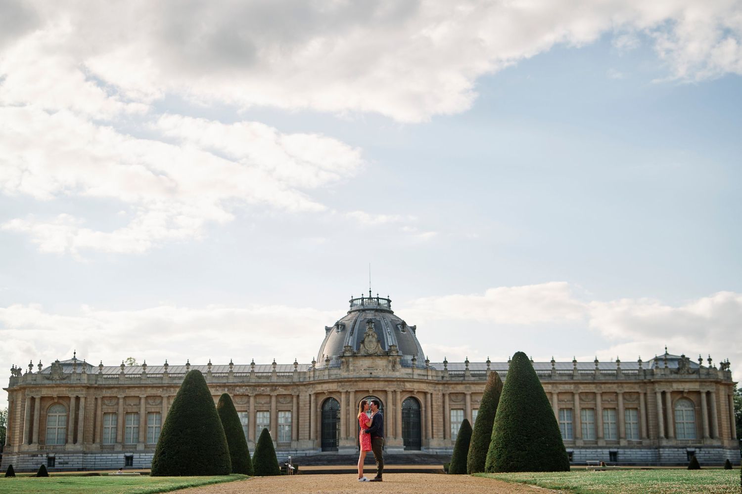 A panoramic view of the Palace of Versailles with its ornate architecture and manicured gardens under a cloudy sky.