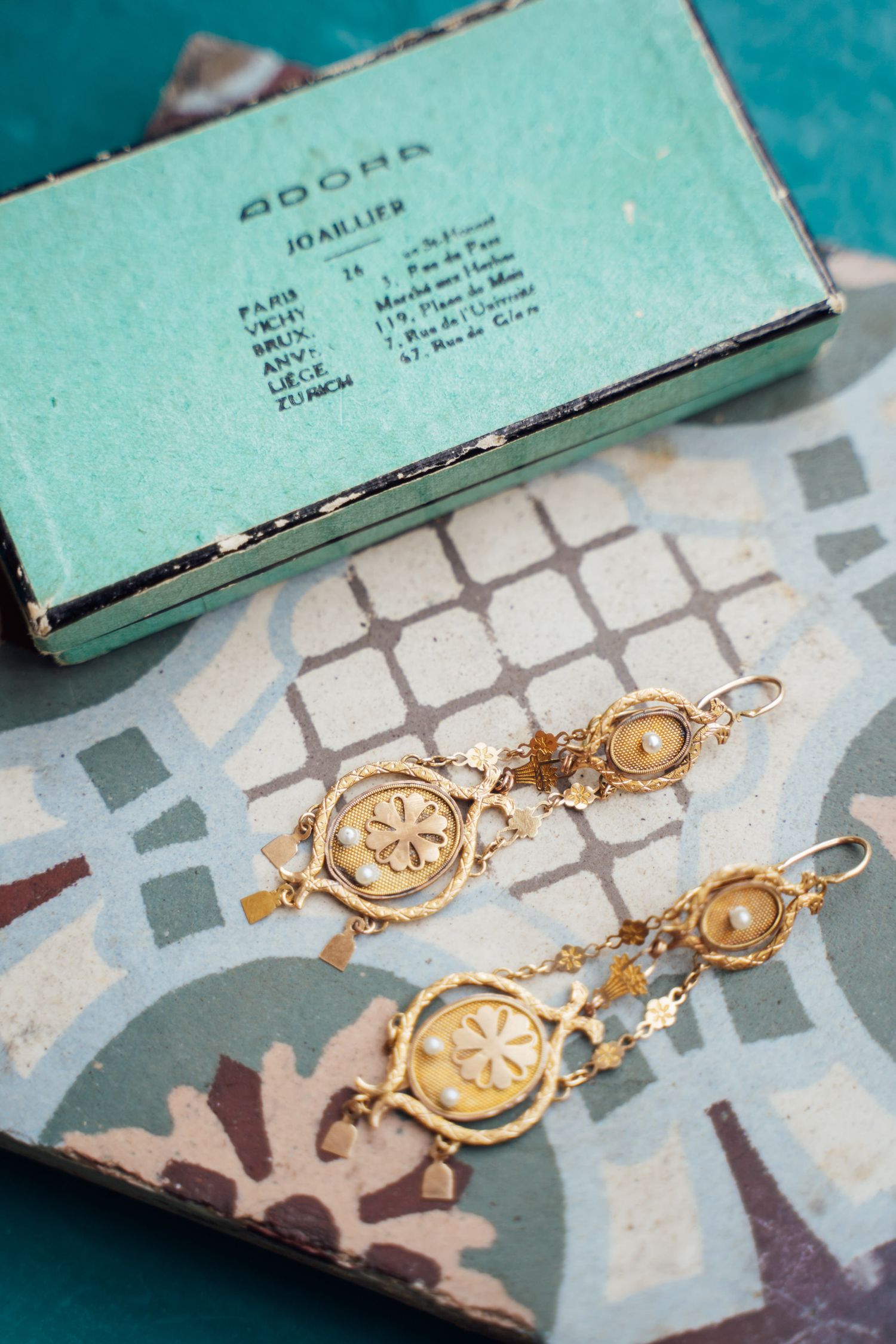Gold earrings with circular designs lay on a turquoise and gray patterned surface with a paper document visible.