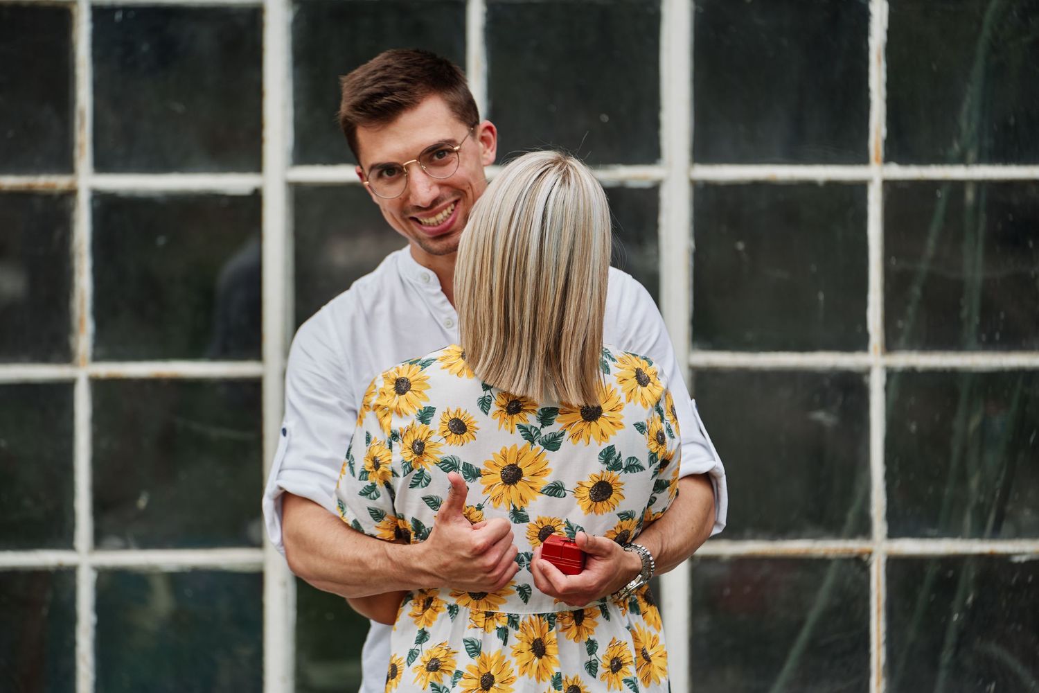 A couple wearing yellow floral outfits embrace and laugh during an outdoor photo session.