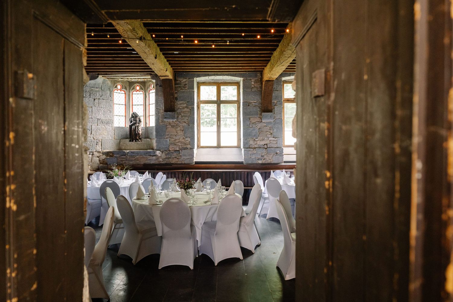Rustic barn interior with white chair covers and tables set up for an elegant wedding reception.
