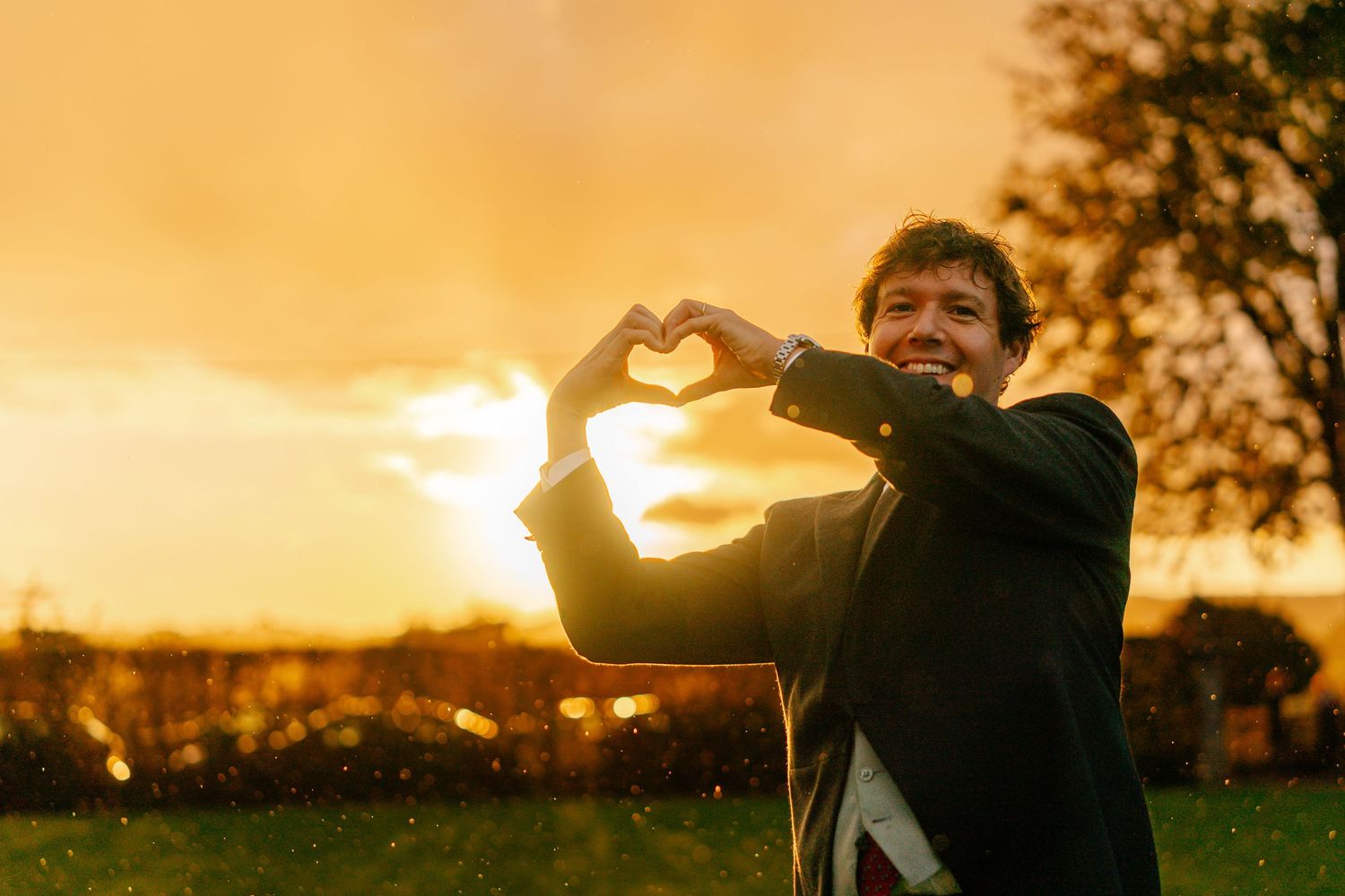 Silhouettes of people making heart shapes with their hands against a vibrant orange sunset sky.