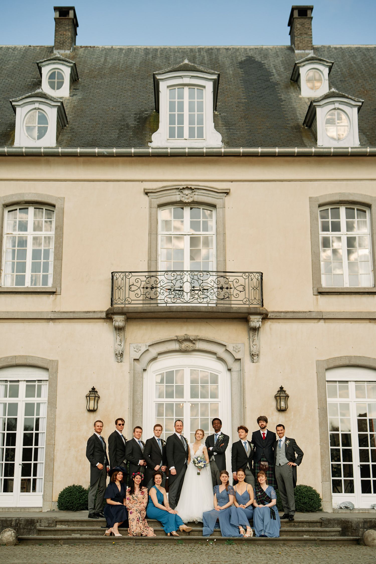 Wedding party poses together on steps of elegant French chateau-style mansion with classic architecture.
