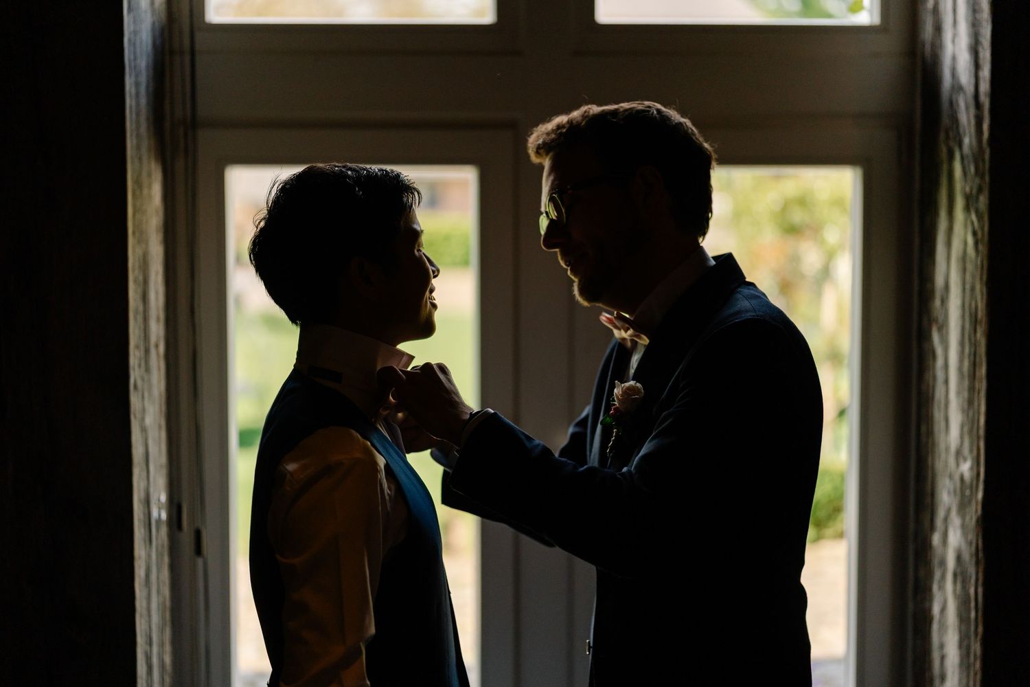 Two silhouetted figures stand in dramatic lighting by a window, with one person gripping the other's collar.