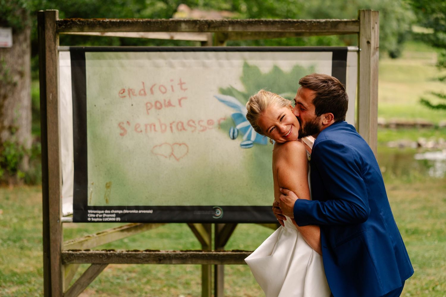 A person in a blue shirt stands in front of a chalkboard while drinking from a water bottle in an outdoor setting.