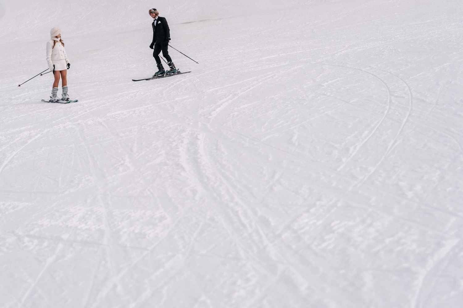 A skier glides down a snowy slope on a sunny winter day with other skiers visible in the distance.