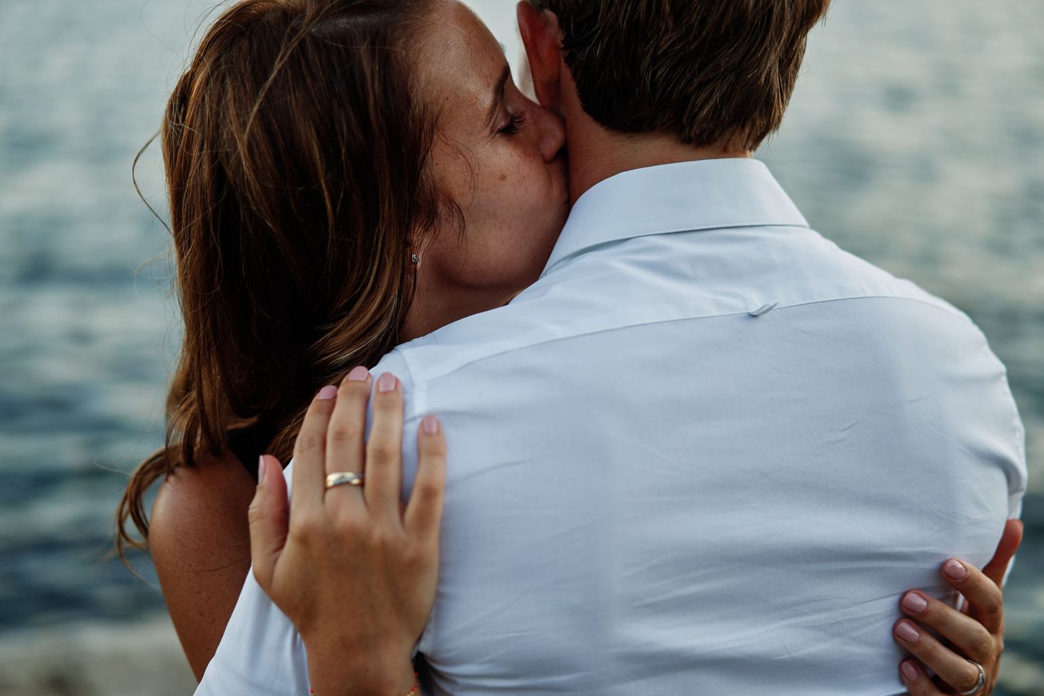A couple embraces while looking out at a scenic ocean view during sunset.