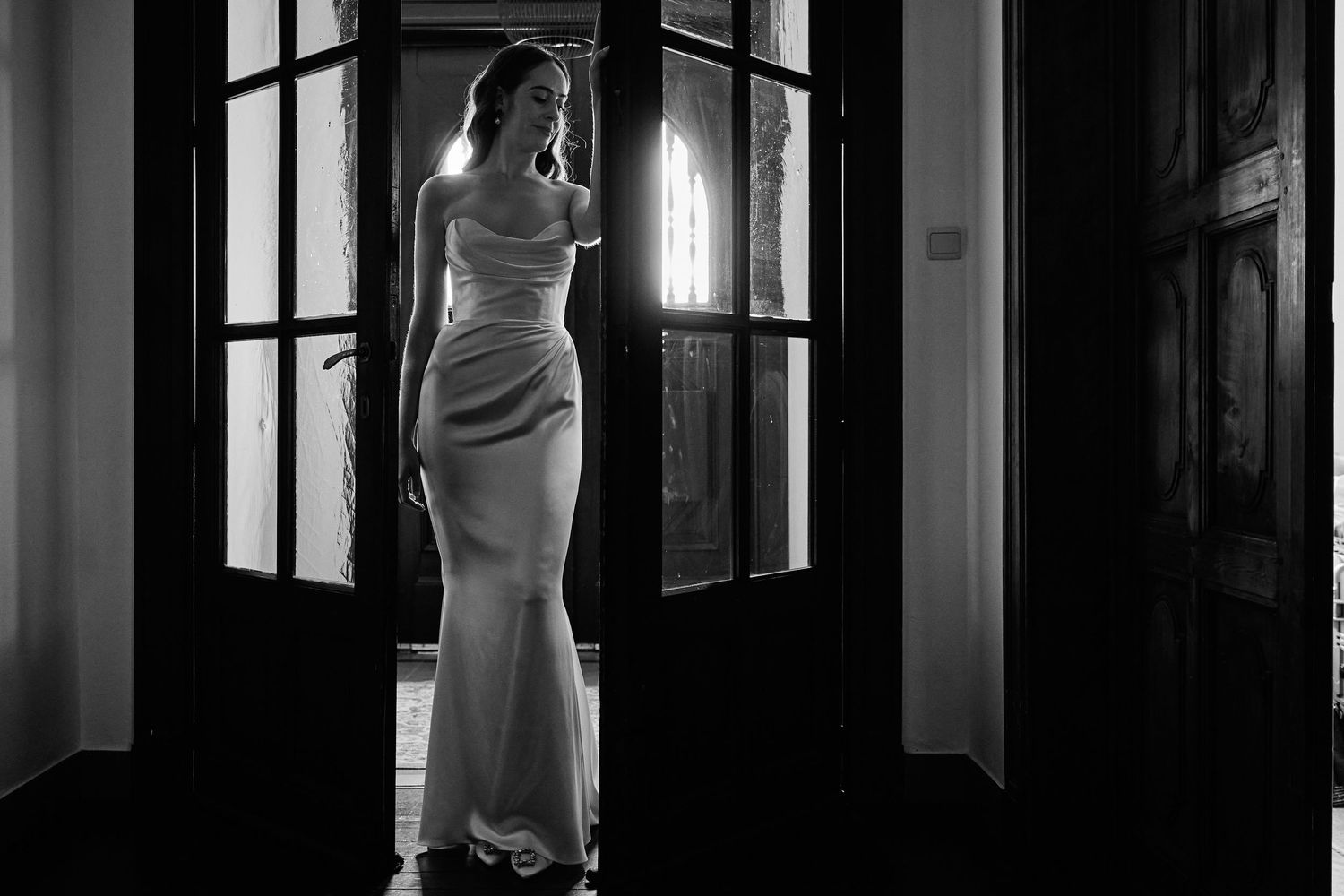 Elegant black and white fashion photograph of a woman in an evening gown standing in a dramatic interior setting.