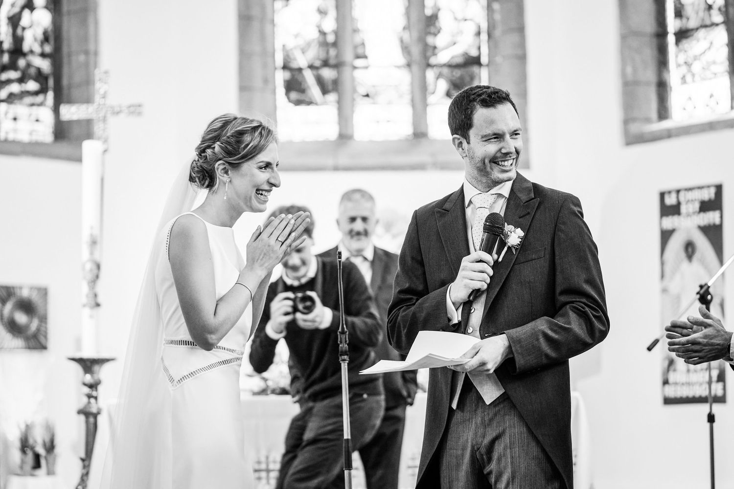 Black and white photo of wedding guests mingling and laughing during an outdoor reception.