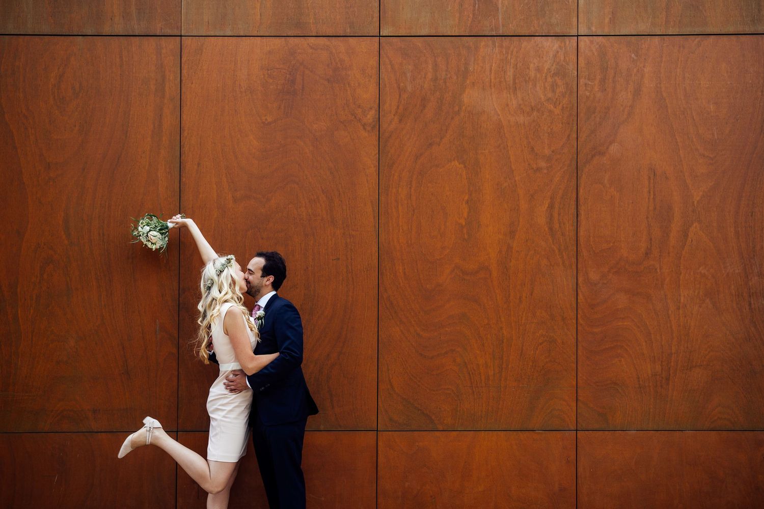 A couple in formal wedding attire dances gracefully in front of a rich wood-paneled wall.