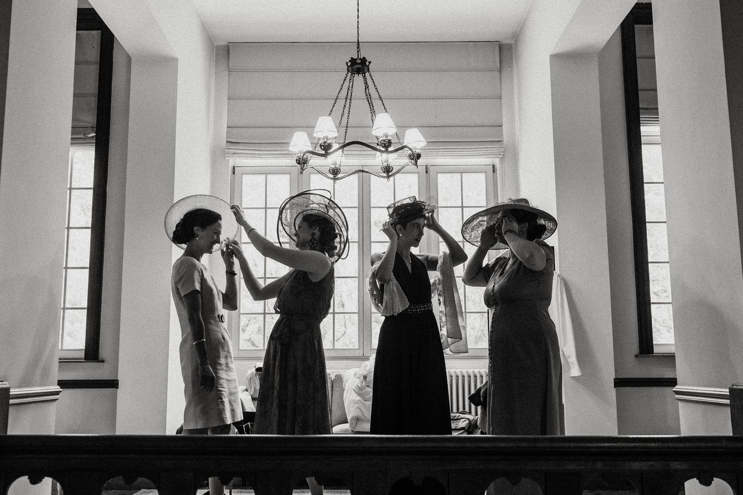 A black and white panoramic photo shows silhouettes of a wedding party in formal attire against bright windows.