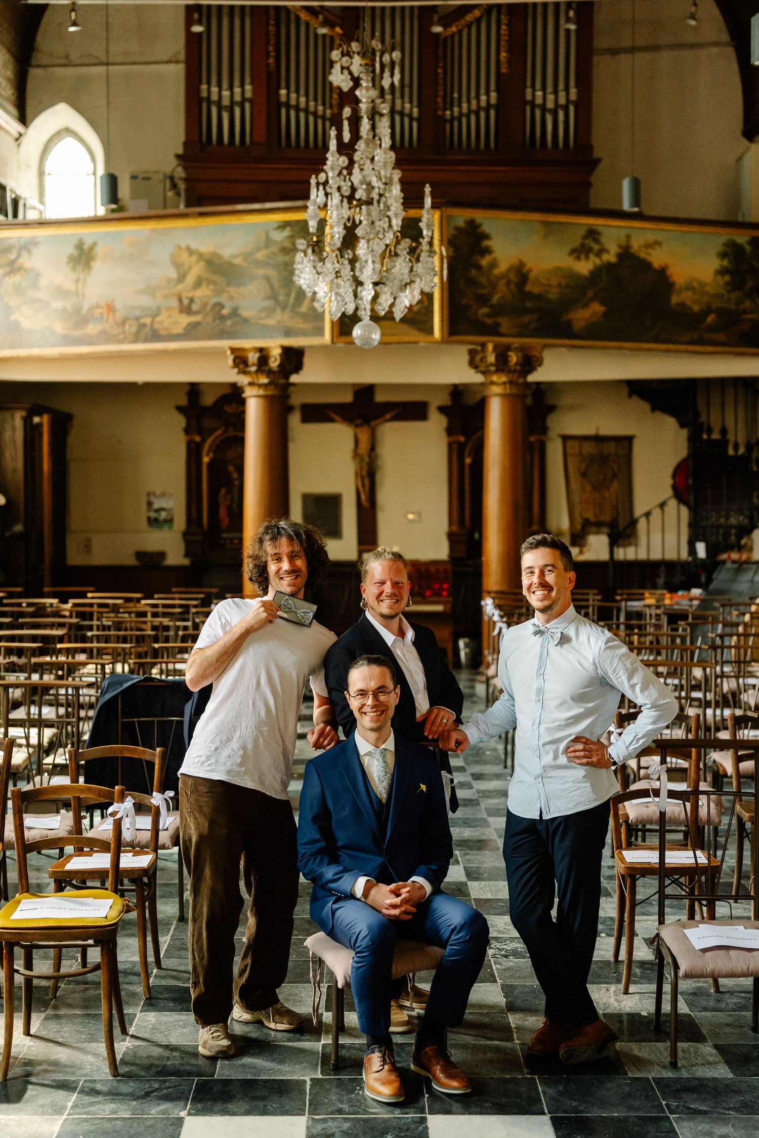 A group of people share joyful moments and laughter while sitting on chairs in an elegant room with columns and chandeliers.