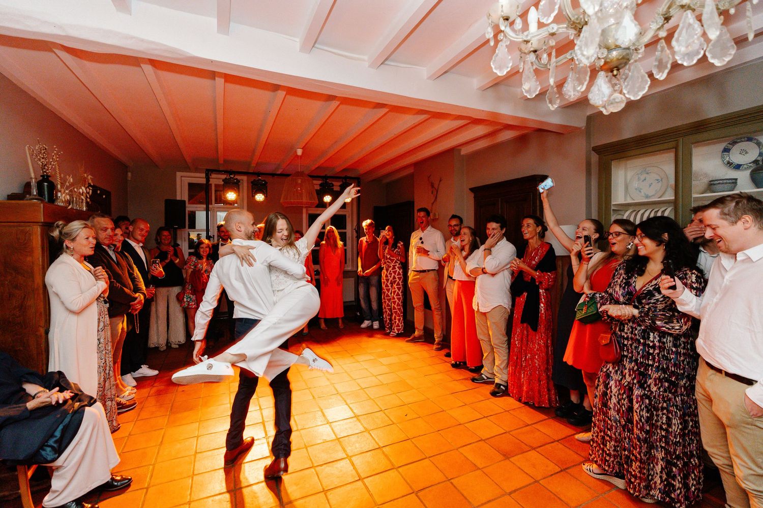 Wedding guests dance and celebrate on a warmly lit ballroom dance floor during an evening reception.