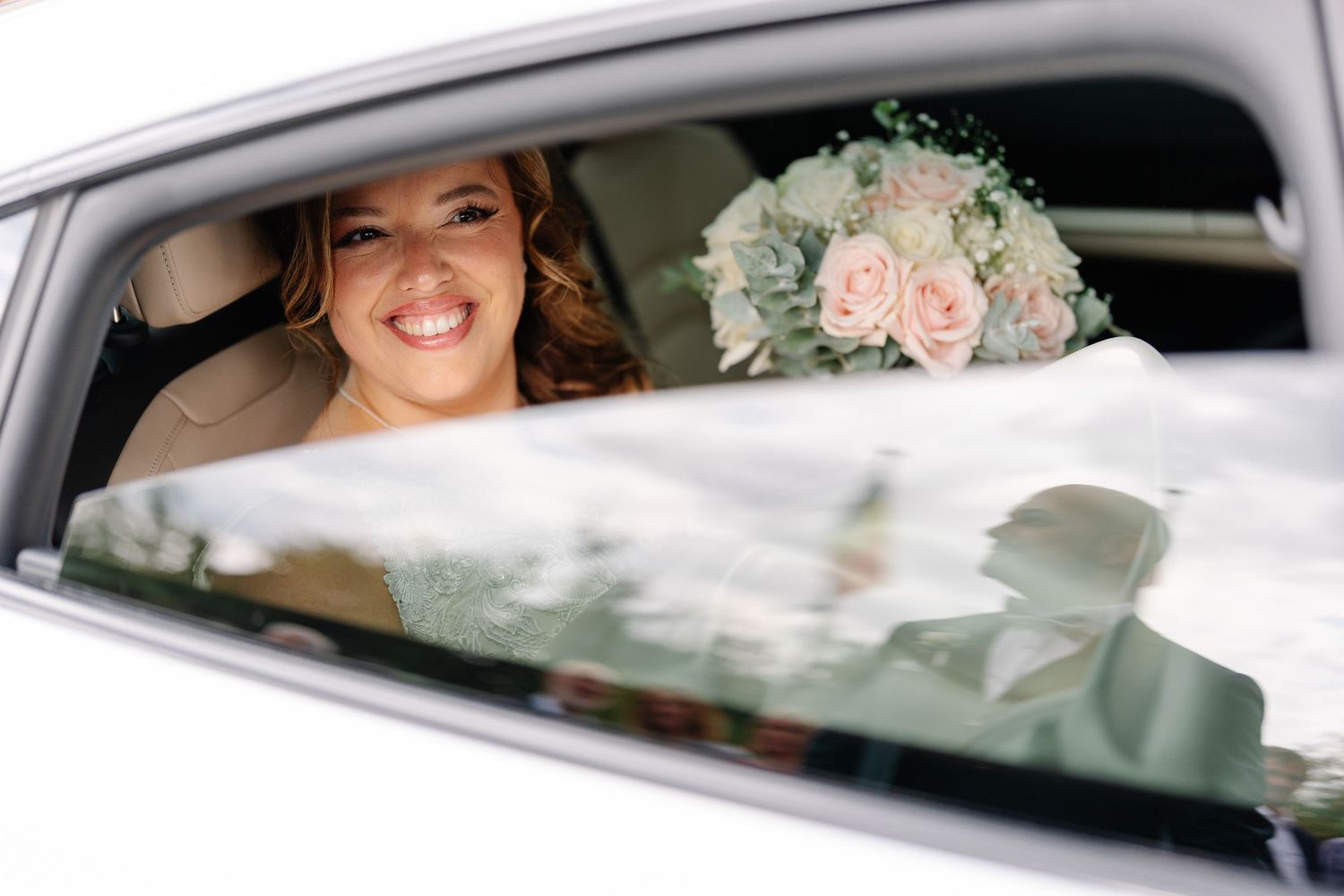 A wedding couple sits in a luxury car decorated with blush pink roses and white ribbons for their special day.