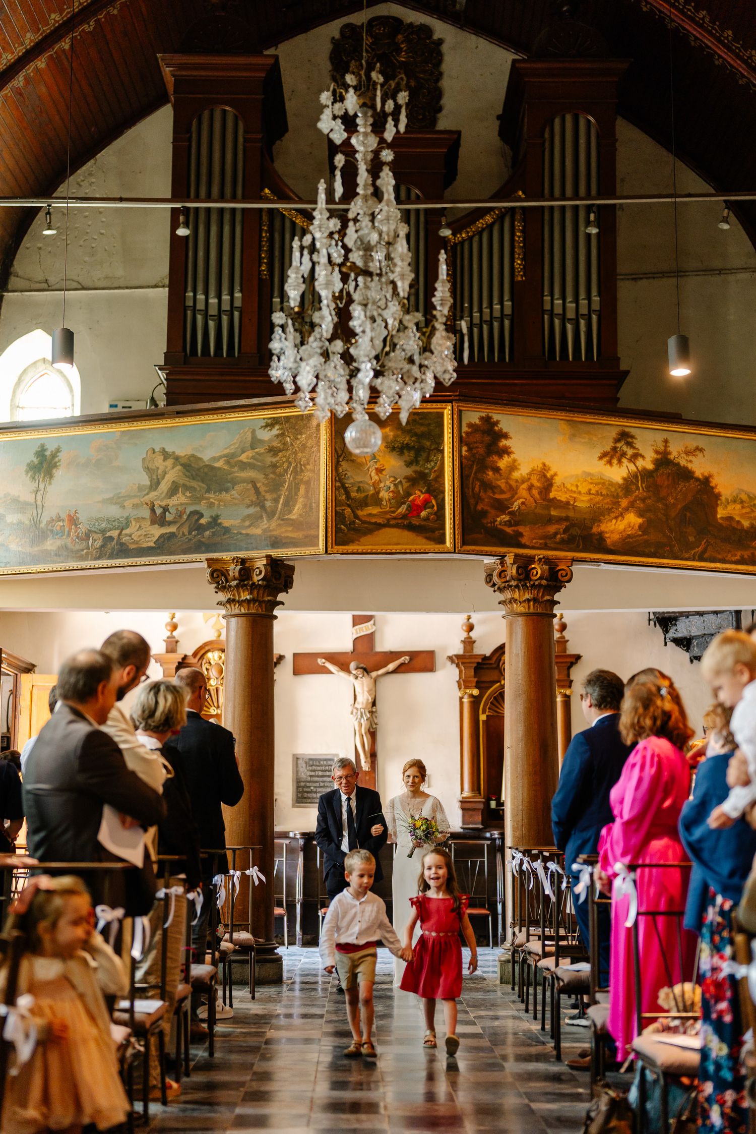 Guests mingle and socialize in an elegant church hall decorated with chandeliers and religious artwork.