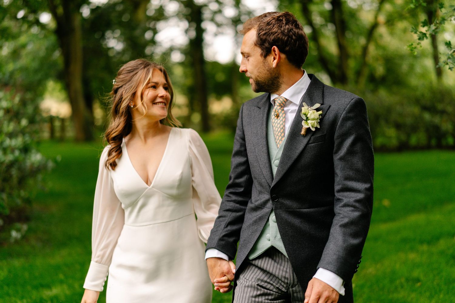 A happy couple in wedding attire walks and laughs together in a lush green garden setting.