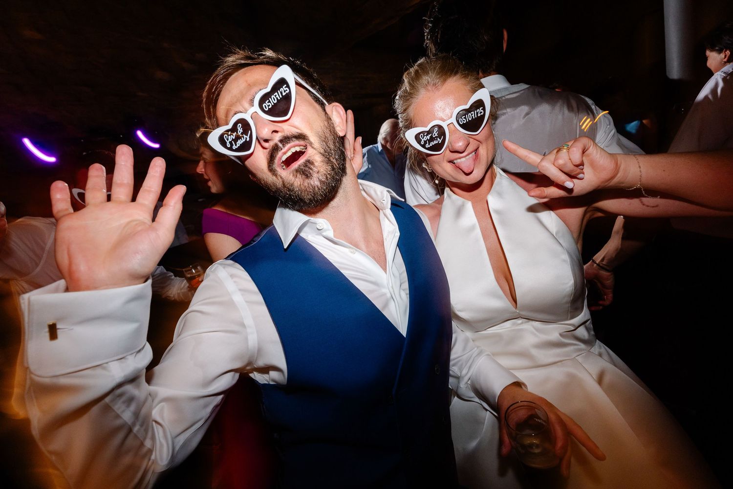 Wedding guests dance enthusiastically on a crowded dance floor during an evening reception celebration.