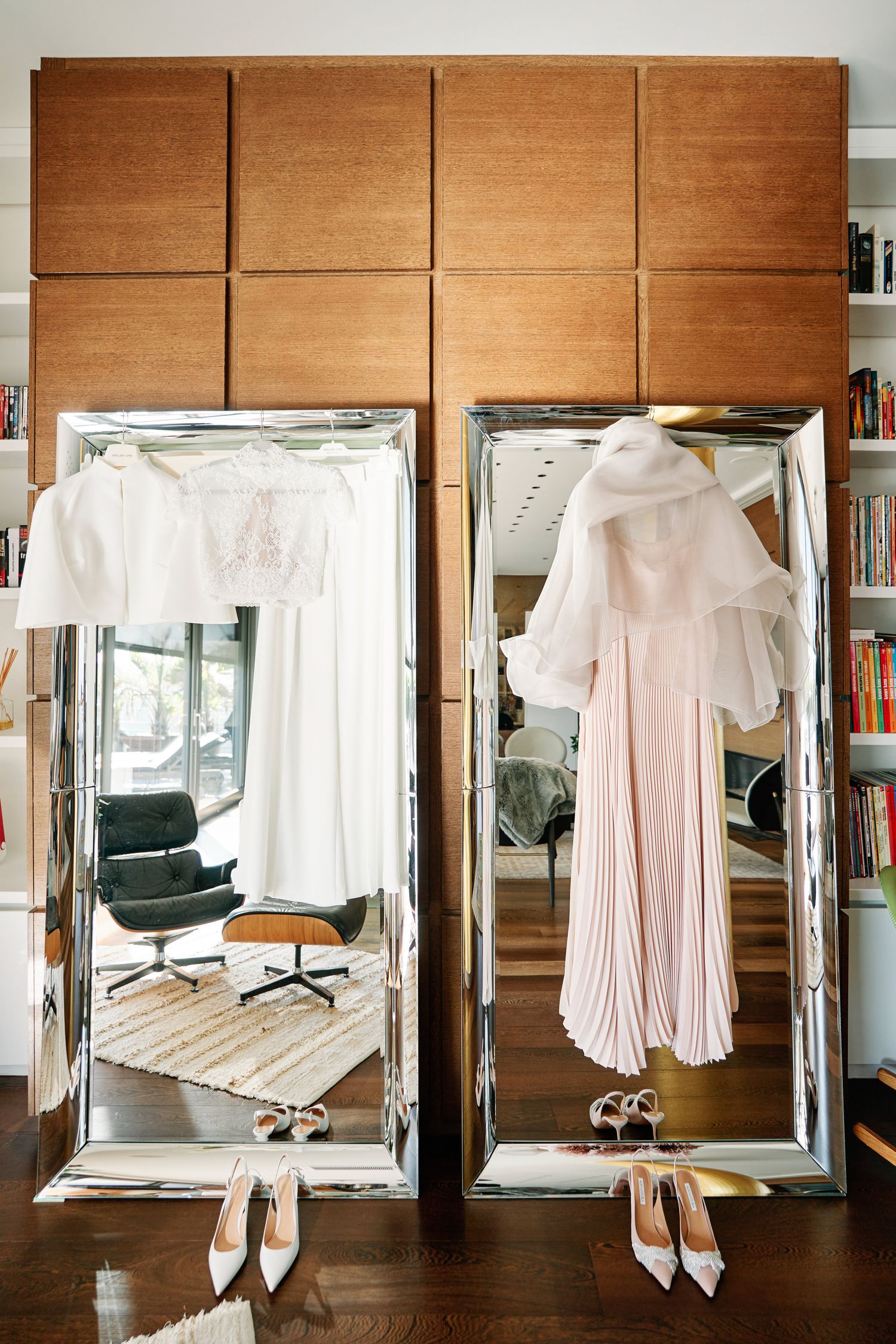 A series of white pleated dresses and garments displayed on hangers against wooden paneled walls in a retail space.
