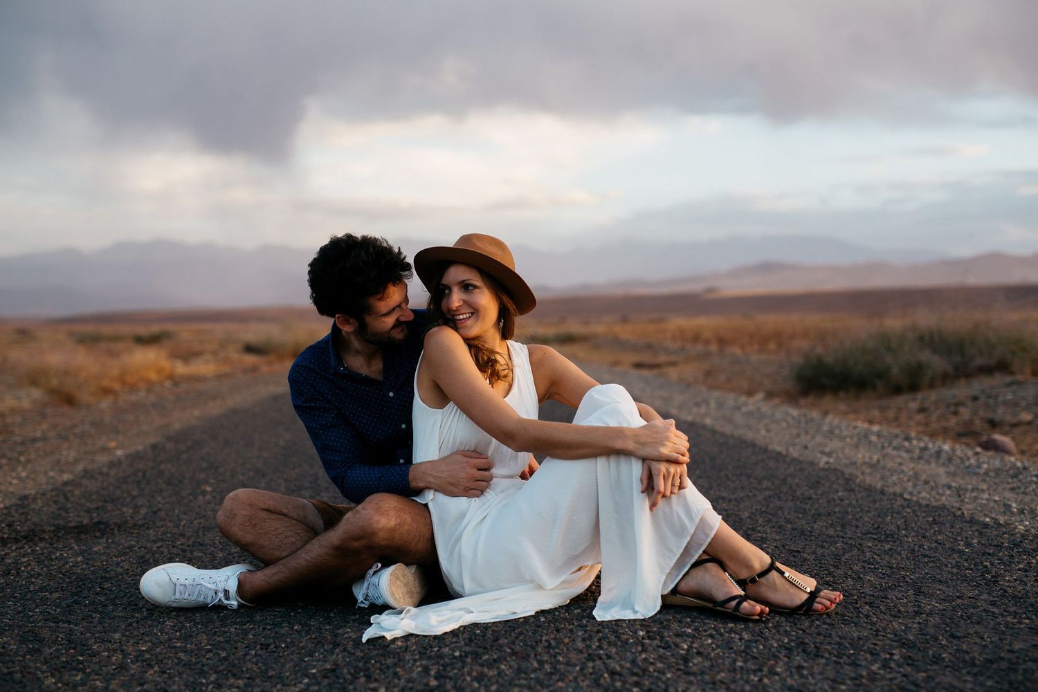 A couple shares an intimate moment together on a dark volcanic beach at sunset with mountains in the distance.