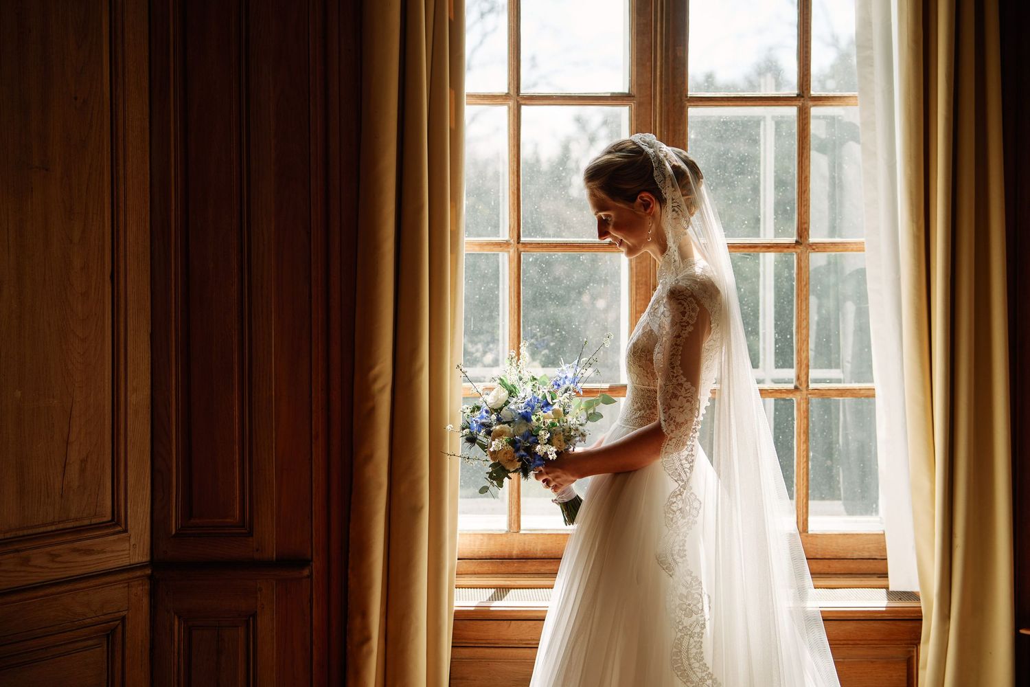 Bright natural light filters through windows in a wood-paneled bridal suite with sheer curtains.