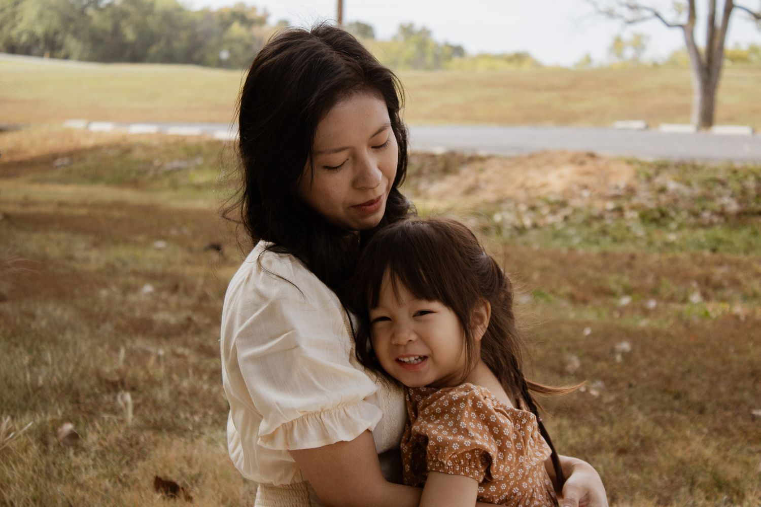 Asian mother tenderly holding her smiling young daughter outdoors in a warm and loving family portrait.