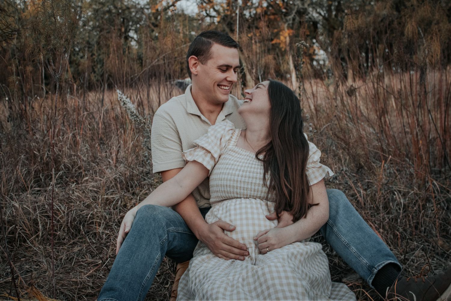 Couple sharing romantic moment sitting in golden field, woman in maternity dress.