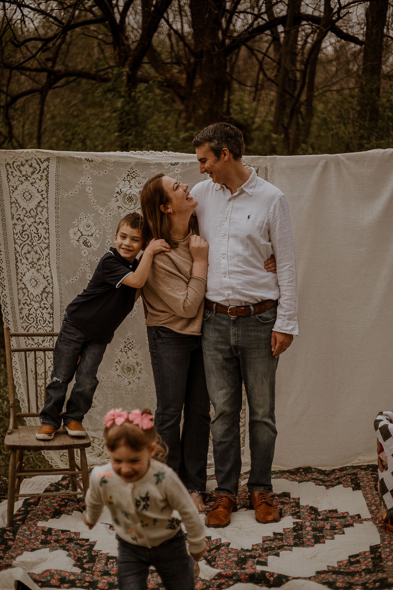 A couple laughs together outdoors while their young children play nearby on a patterned rug.