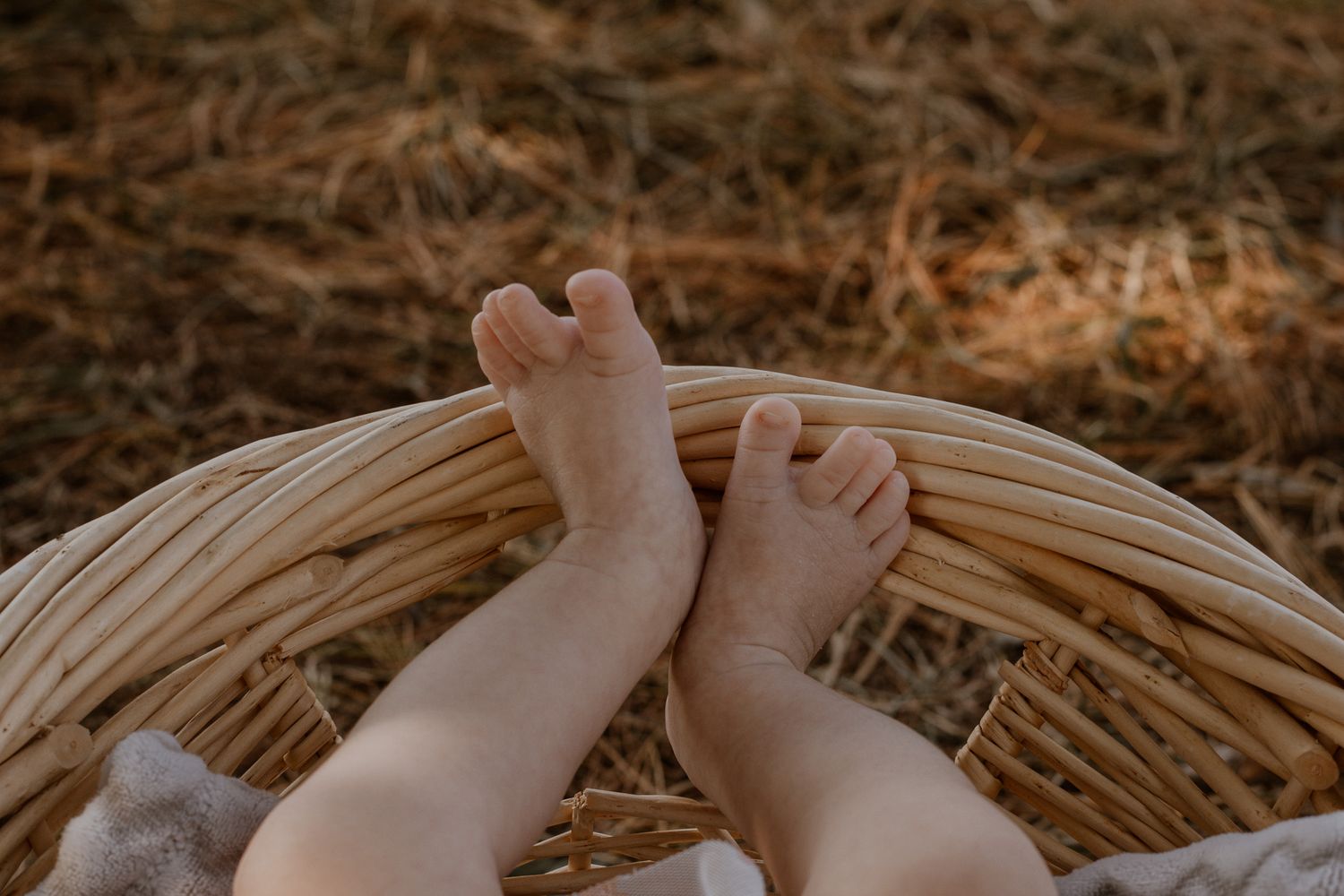 Tiny baby feet resting on the edge of a wicker basket outdoors.