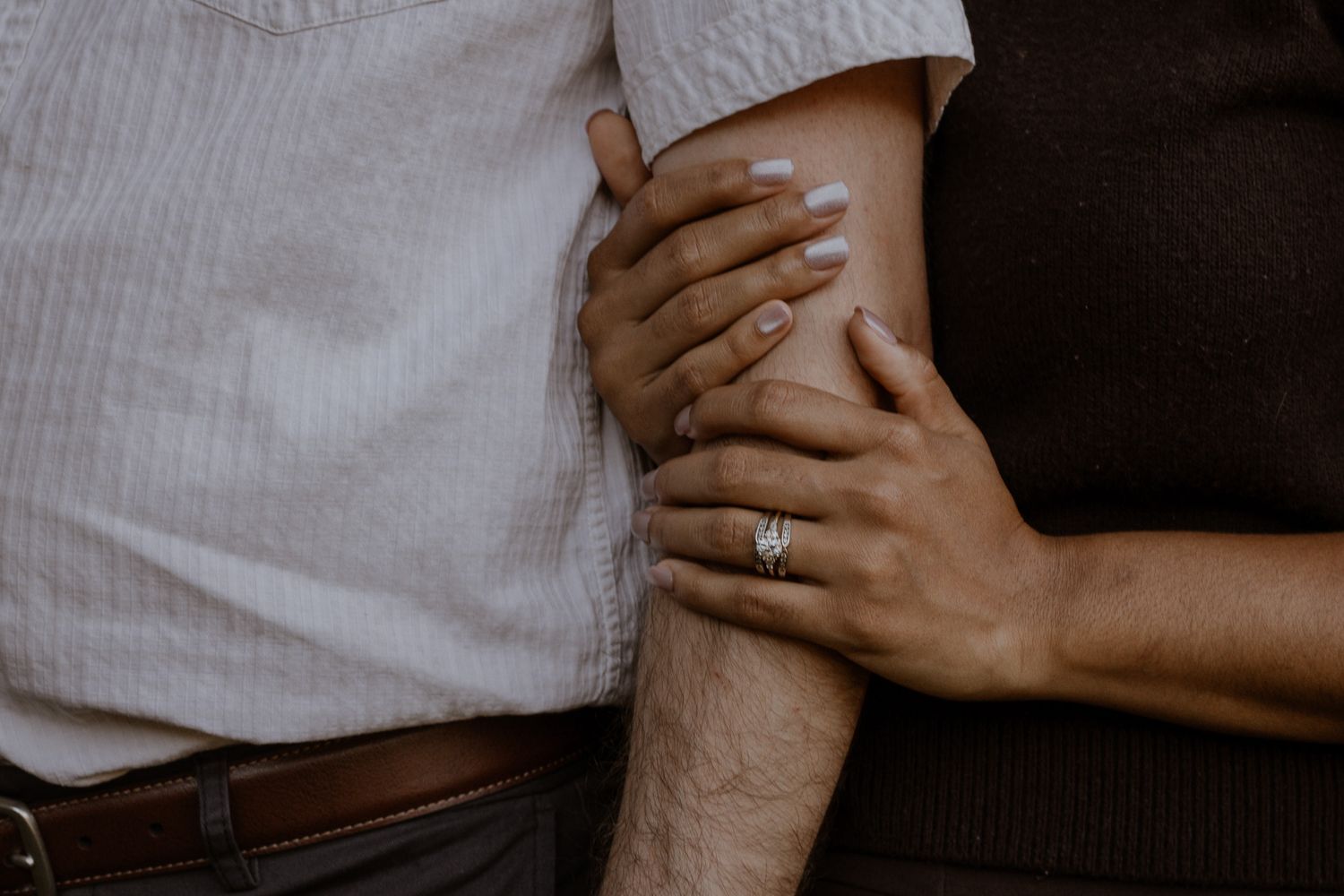 Close-up of a couple holding arms together, woman wearing a sparkling diamond engagement ring.