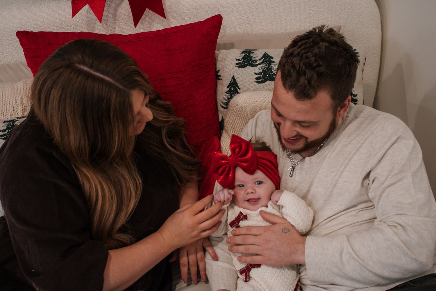 Happy parents smiling at their newborn baby with a red bow during a Christmas photo session.