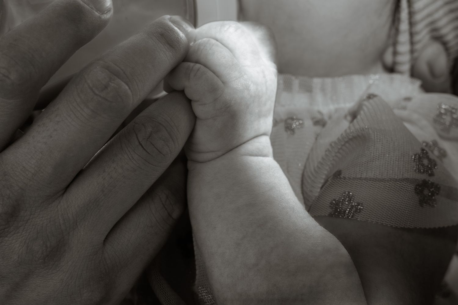 Black and white close-up of a newborn baby grasping an adult finger with tiny hand.