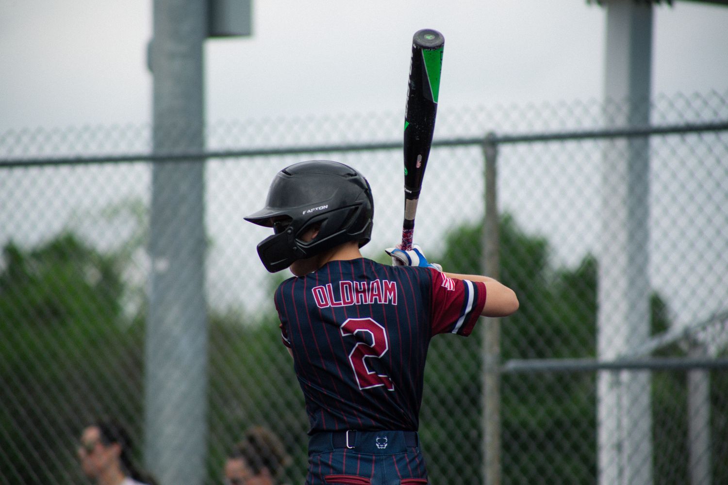 Youth baseball player #2 Olguin stands at bat in a dark jersey, helmet on, ready to swing at an outdoor game.