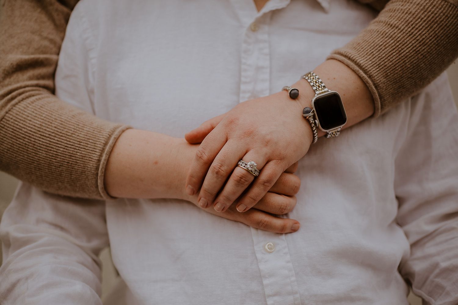 Close-up of couple holding hands, woman wearing diamond engagement ring and Apple Watch with silver band.