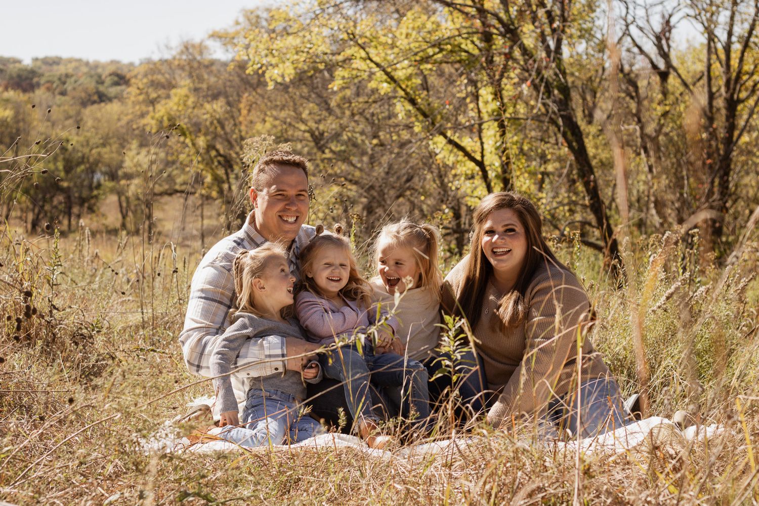 Happy family of five sitting together in a golden autumn meadow surrounded by fall foliage.
