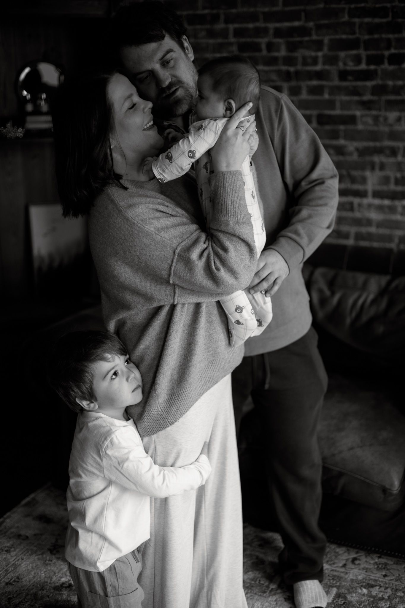 A black and white photo series shows a child hugging someone in a sweater against a brick wall background.