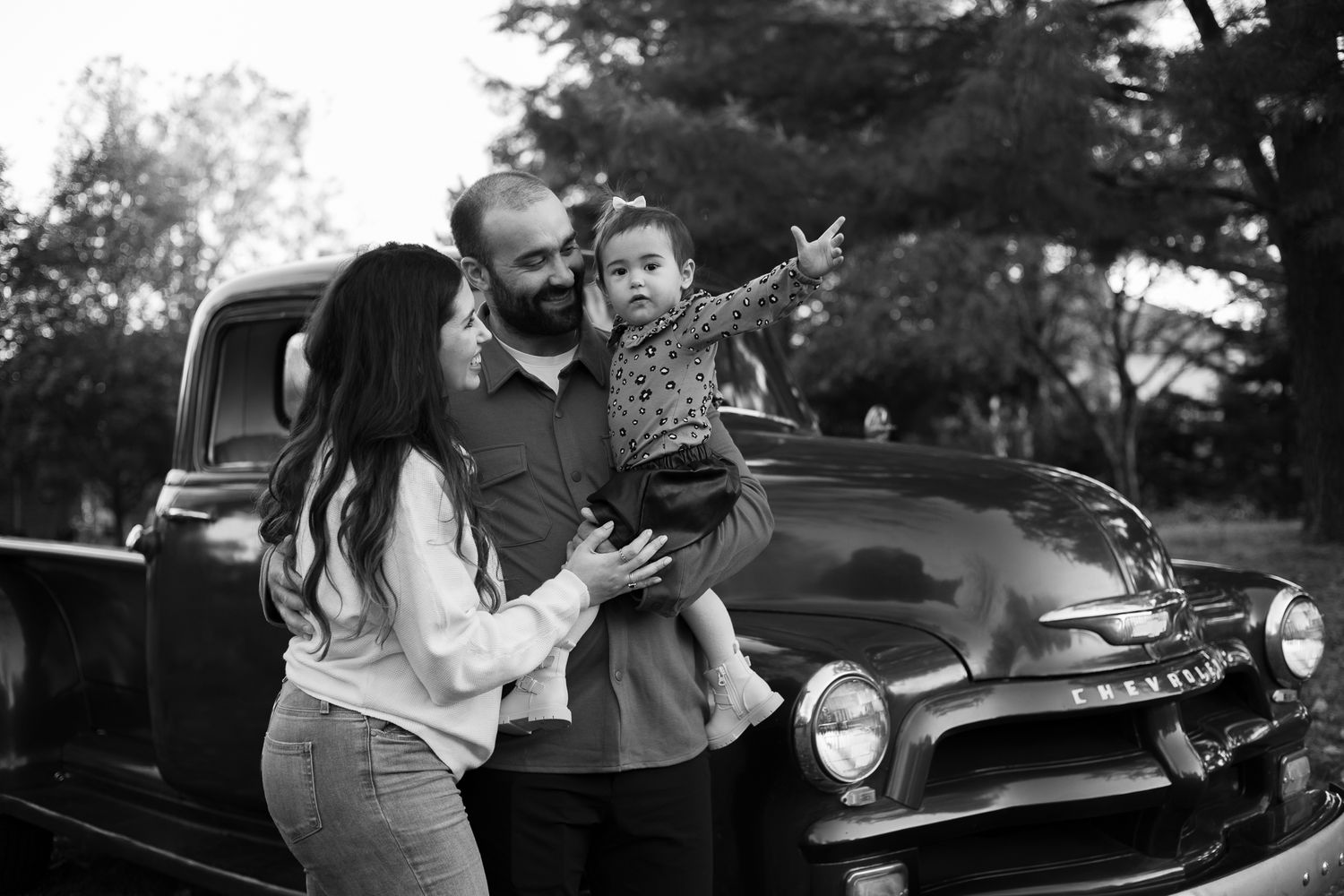 A romantic black and white engagement photo session featuring a couple embracing near a vintage car.