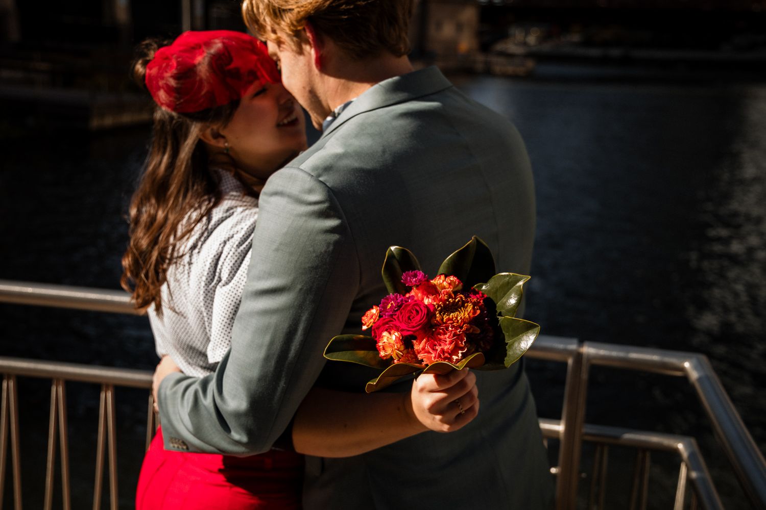 Couple in a romantic dance pose with red flowers against a dark background.