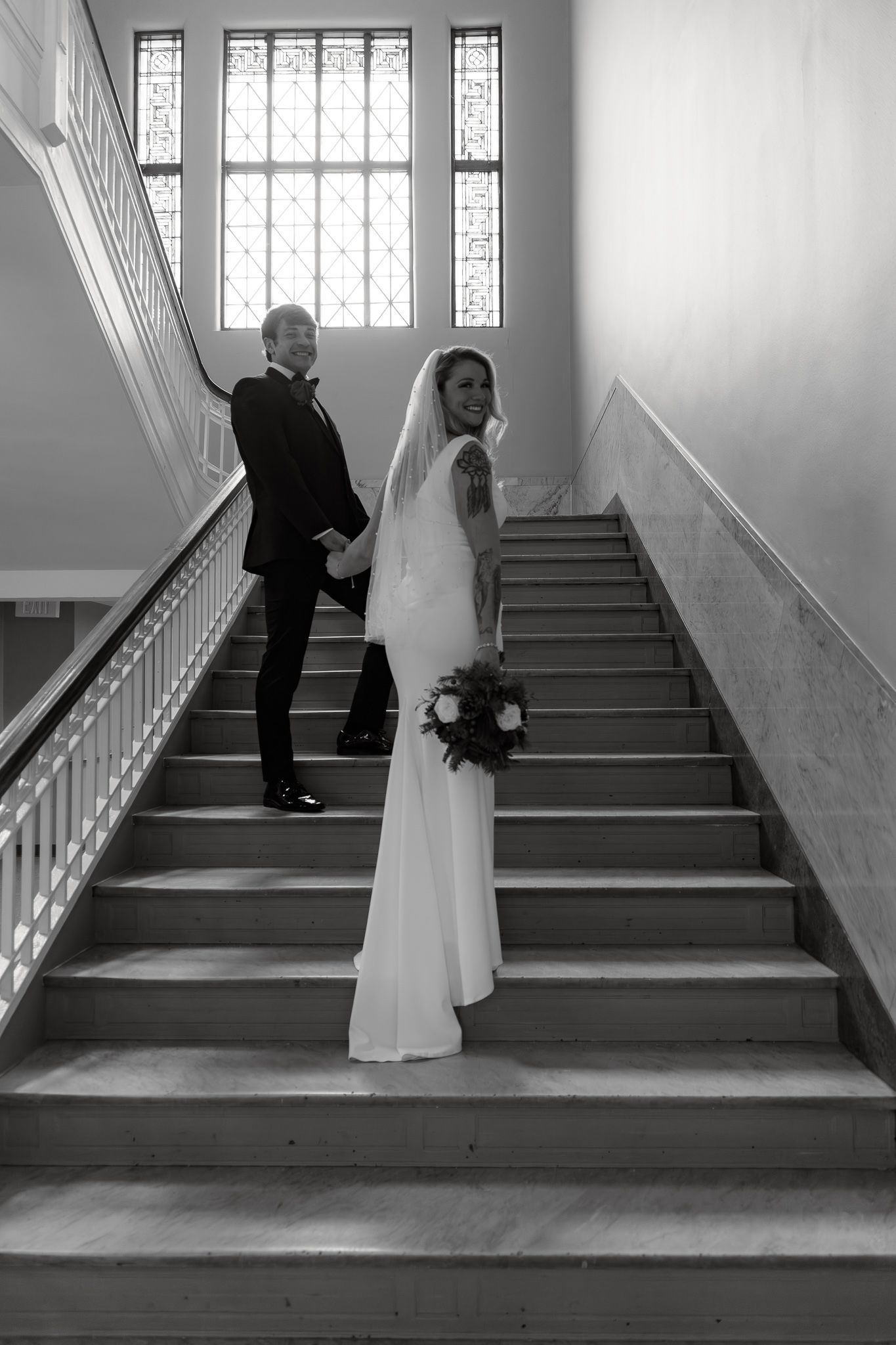 A sequence of black and white photos showing a couple ascending a staircase in a church with stained glass windows.