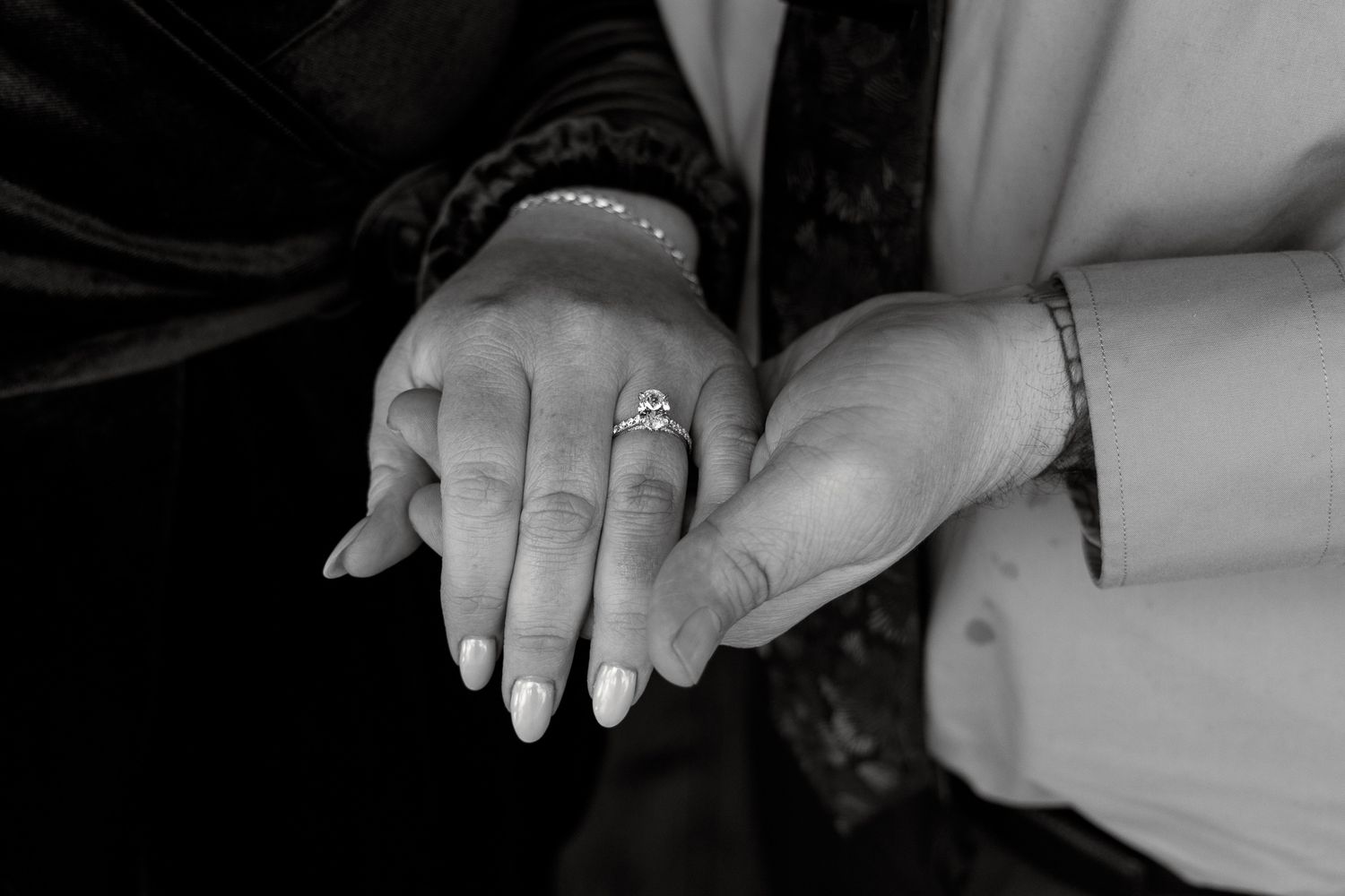 Close up black and white photo of hands with wedding rings and jewelry.