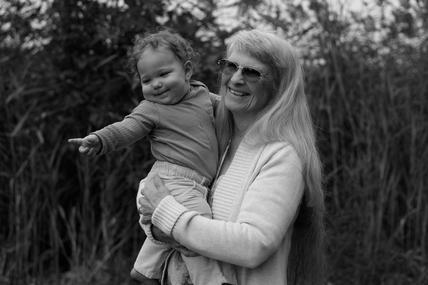 A black and white portrait of a parent and young child smiling together outdoors.