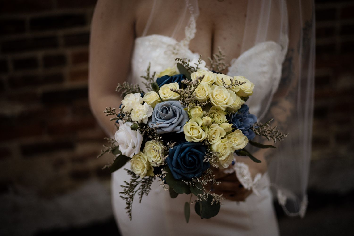 A close-up view of a bridal bouquet featuring yellow roses, blue flowers and delicate foliage.