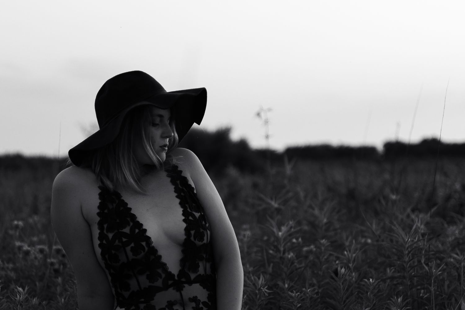 Black and white portrait of person in hat sitting in wildflower field.