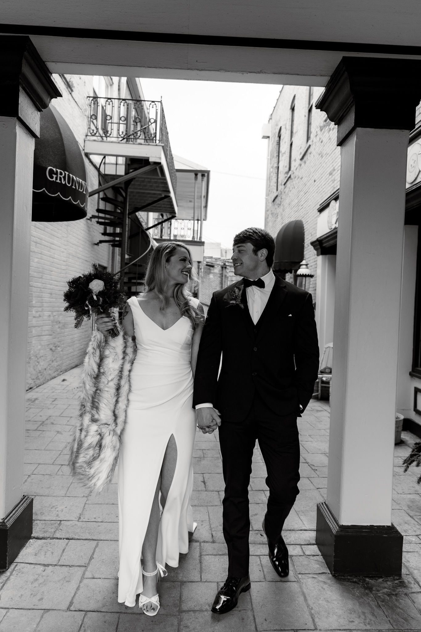 Black and white wedding sequence shows couple walking under covered walkway with bride's dress trailing behind them.