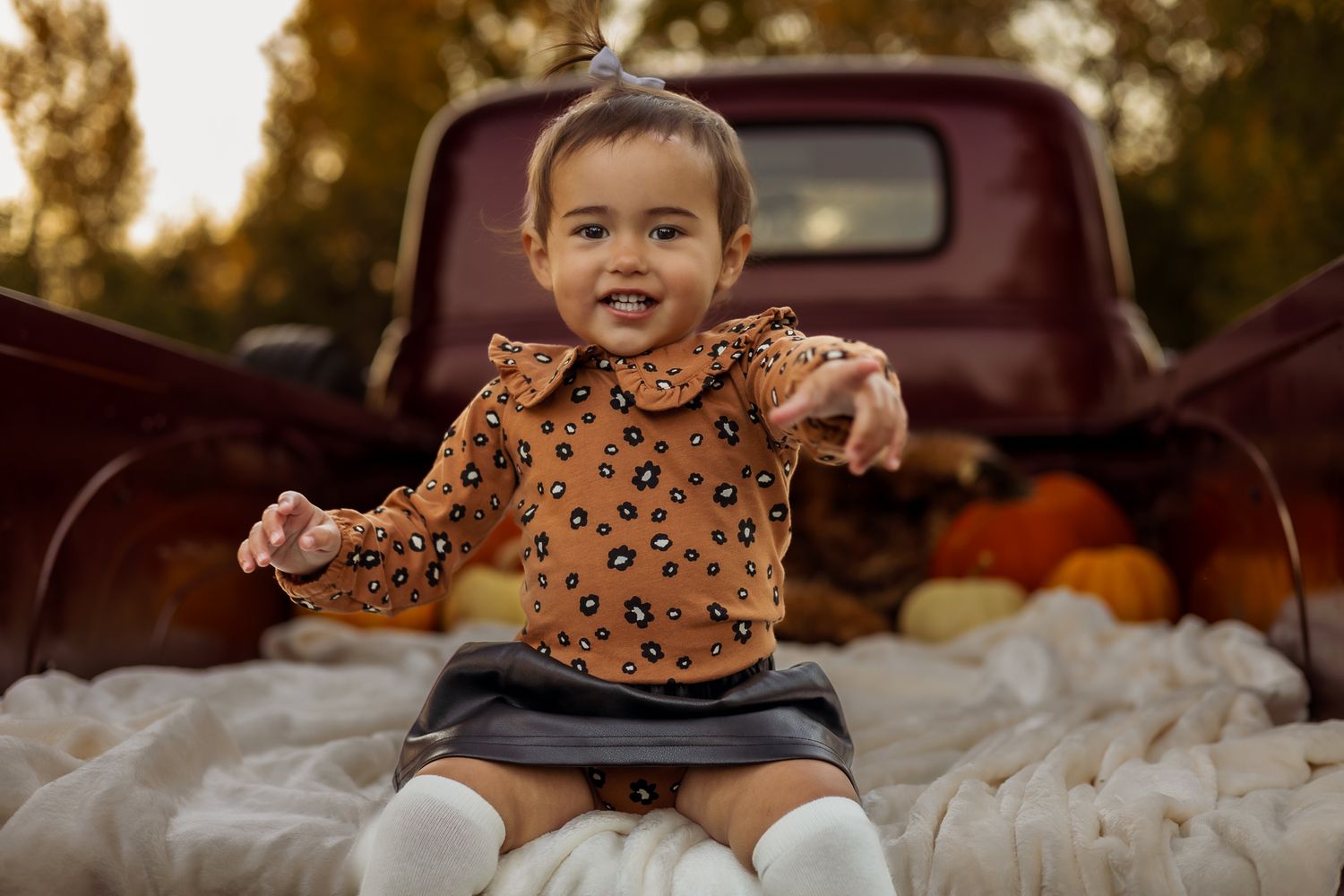 Joyful child in orange patterned sweater poses energetically in rustic truck bed with autumn decorations.