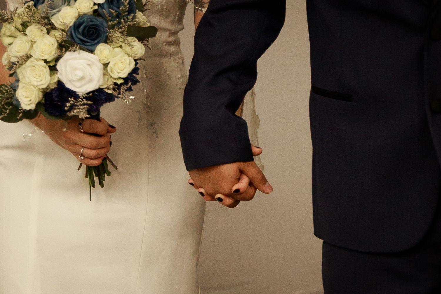 A close-up view of a bridal bouquet featuring white roses and dark greenery against a formal wedding attire background.