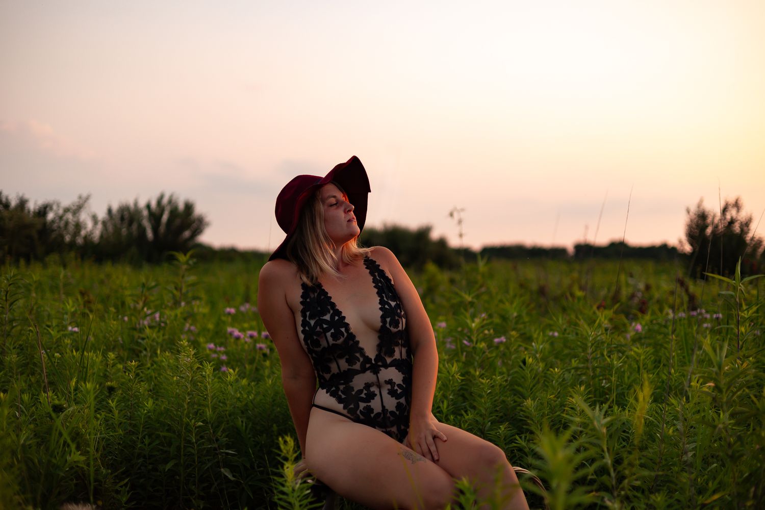 Person in swimsuit sitting in wildflower field at sunset.