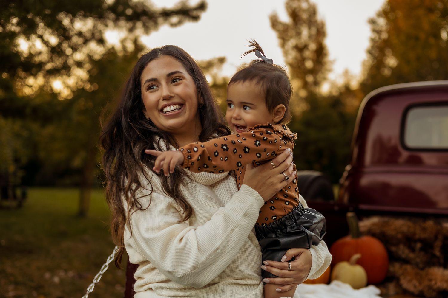 A parent and child share joyful moments together during a golden sunset photoshoot near a vintage red truck.