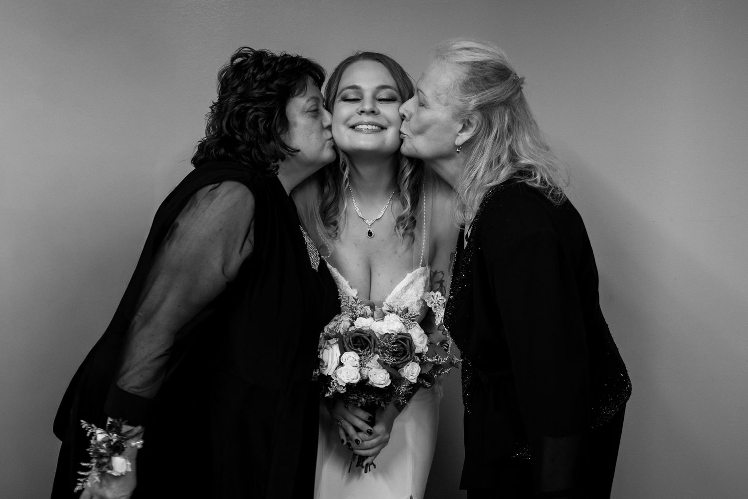 A black and white portrait of three people sharing an intimate moment with a bridal bouquet.